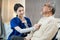 Asian nurse at nursing home taking care of senior man on wheelchair. Young woman therapist doctor measure heart rate by