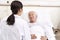 Asian old man lying in bed talking to young female doctor in hospital ward