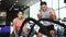 Asian personal trainer coaching a bodybuilding woman to perform crossfit battle ropes exercise in the fitness gym