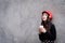 Asian portrait woman with red hat and black clothes has holding a cup of coffee with happiness and the grey stone wallpaper