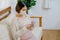 Asian pregnant woman with mask look at mobile phone and sit on sofa in living room of her house with soft light