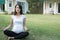 asian pregnant woman practicing yoga while sitting in lotus position on green grass in front of her house. meditating on