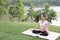 asian pregnant woman practicing yoga while sitting in lotus position on green grass in public park. meditating on maternity.