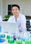 Asian professional cheerful male scientist researcher in white lab coat rubber gloves sitting smiling typing data in laptop