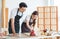 Asian professional male carpenter in apron complimenting showing thumb up to female lover worker using polishing machine rubbing