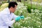 Asian scientist man with white lab gown analysis and record the data of white and multicolor flowers in the garden during day time