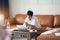 Asian self employed woman sitting on couch thinking & working on laptop at home