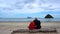 Asian senior couple sitting hugging at beach front waring mask new normal stress release trip