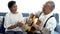 Asian senior couple sitting on the sofa and playing acoustic guitar together. Happy smiling elderly woman clapping hands