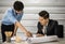 Asian senior good-looking boss in suit sitting at desk and working with junior employee in office with roll of paper. Businessmen