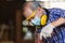 Asian senior man carpenter wear protective mask dust and headphone working with electrical drill to drill a hole wood.