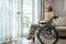 Asian senior man disabled sitting alone in wheelchair looking through window at hospital