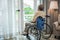 Asian senior man disabled sitting alone in wheelchair looking through window at hospital