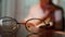 Asian senior reading a book on the bed in room at night. Selective focus through glasses on table.