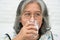 Asian Senior woman holding glass milk while relaxing on a sofa living room for retirement wellness. Elderly Woman drinking a glass