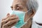 Asian senior woman in a medical mask,elderly patient covering nose and mouth with her hand while coughing or sneezing,prevent the