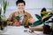 Asian short hair woman smiling and holding plant pot To write down reports on the growth of potted plants on his desk with home