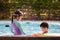 Asian sibling girl and boy playing water with toy together in the swimming pool with fun.