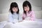 Asian sibling girls in pajamas watching smartphone on a bed at night. mobile addiction technology concept