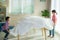 Asian siblings sister and brother stretching a white blanket over table furniture to make a fort in living room at home for