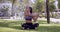Asian sportive woman sitting with crossed legs and stretching arms in park