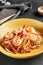 Asian Stir Fried Shrimp and Rice Noodles. Sesame Rice Noodles with Shrimp in yellow plate with wooden chopstick on dark slate