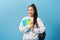 Asian student with backpack holding notebooks against light blue background