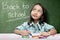 Asian student girl drawing on white paper with colorful crayons over chalkboard background