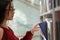 Asian student girl picking up book from shelf while standing between library bookcases