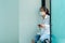 Asian teenage girl wearing white shirt Leaning against a white wall, pressing a cell phone with a medical mask covering his mouth