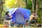 Asian teenager playing guitar front of blue canvas camping tent on grass field smile happy face