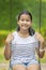 Asian teenager toothy smiling face and sitting on swing in green