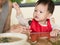 Asian toddler learn to eat meal herself holding chopsticks.