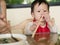 Asian toddler learn to eat meal herself holding chopsticks.