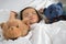 Asian toddler sleeping with teddy bear on white bed, pillow and sheet