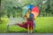 Asian transgender university student holding rainbow pride umbrella sitting on bench at campus park