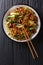 Asian vegetarian food udon noodles with baby bok choy, shiitake mushrooms, sesame and pepper close-up on a plate. Vertical top