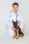 Asian vet in a white coat with a stethoscope on his neck examines a German shepherd puppy on a table in a veterinary clinic.