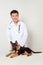 Asian vet in a white coat with a stethoscope on his neck examines a German shepherd puppy on a table in a veterinary clinic.