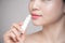 Asian woman applying hygienic lip balm over grey background