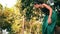 An Asian woman approaches someone with an angry expression while wearing green clothes and makeup in the middle of the forest