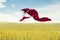 Asian woman ballerina holding red fabric making a big jump on meadow.