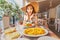 Asian woman in big hat having meal with greek salad Horiatiki in restaurant. Greece cuisine concept