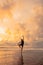 An Asian woman in a black dress performs ballet movements beautifully on the beach with waves and clouds behind her