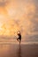 An Asian woman in a black dress performs ballet movements beautifully on the beach with waves and clouds behind her