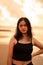 An Asian woman in a black shirt with an expression that looks annoyed is standing near the waves on the beach in a holiday