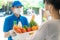 Asian woman costumer wearing face mask and glove receive groceries box of food, fruit, vegetable and drink from delivery man   in