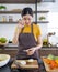 Asian woman crying while holding a piece of onion. Young housewife slices onion into pieces on a wooden chopping board. Morning