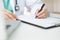 Asian woman Doctor with green cloth and lab coat working and taking note information of patient in checklist paper on clipboard in