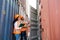 asian woman Engineer with note clipboard and asian man Supervisor in Hard Hats and Safety Vests Stand in Container Terminal.